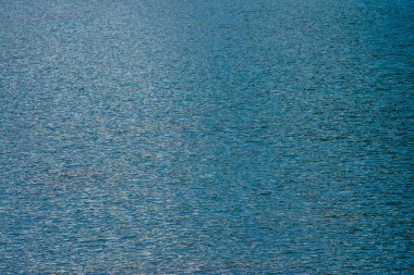 Akşam sakin kobalt temiz su yüzeyinin inanılmaz dokulu arka plan. Güneş ışığı dağ gölüne yakın olarak yansıdı. Sabahları parlak mavi suda güzel dalgalar. Harika rahatlayın doku.