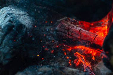 Yanmış odunlar yakın çekim ateşinde yanmış. Atmosferik arka plan ve kamp ateşi. İçeriden kopyalanmış şenlik ateşinin tasavvur edilemez detaylı görüntüsü. Duman fırtınası ve parlayan közler..