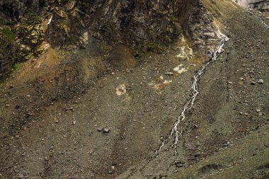 Gevşek taşlardan eğim ayrıntılı doğal doku. Dağ suyu akıntısı dağ yamacından aşağı akar. Kayanın üzerinde küçük bir şelale. Görkemli doğanın sıradışı manzara.