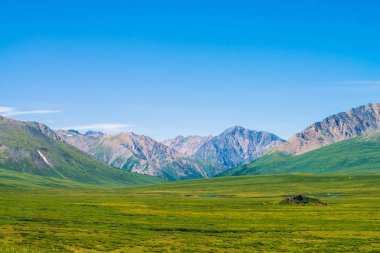 Berrak mavi gökyüzü altında yeşil vadi üzerinde kar ile dev dağlar. Zengin bitki örtüsü ve güneş ışığında dağlık göller ile Çayır. Görkemli doğanın inanılmaz güneşli dağ manzara.