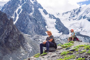 Gezginler buzulun yakınındaki tepede dinlenirler. Harika dev karlı dağlar. Dağlık arazide yürüyüş. Görkemli doğanın inanılmaz atmosferik dağ manzarası. İnsanlar yükseklere tırmanıyor. Sırtta kar.