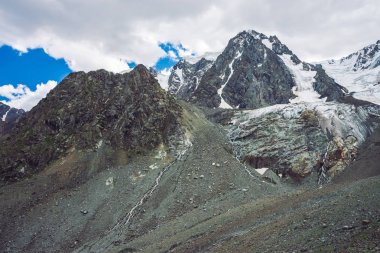 Atmosferik dev karlı dağlar. Şelaleli buzlu kayalar. Buzuldan su akışı. Buzlu koyu kayalık dağ yamacı. Dağ sırtında kar. Yaylaların görkemli doğasının sıradışı manzarası.