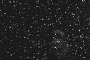Yağmur damlalarıyla kirli pencere camı. Yağmur damlaları ile atmosferik tek renkli koyu arka plan. Damlacıklar ve lekeler kapanır. Kopyalama alanı ile makroda ayrıntılı saydam doku. Gece yağmurlu hava.