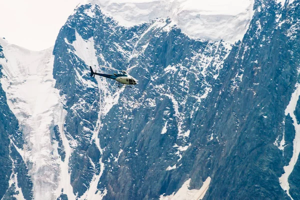 Helicopter in air against background of snowy mountain. Rescue mission in glaciers to rescue climbers. Aerial tourism in highlands in overcast weather. Atmospheric view on icy rock close up.