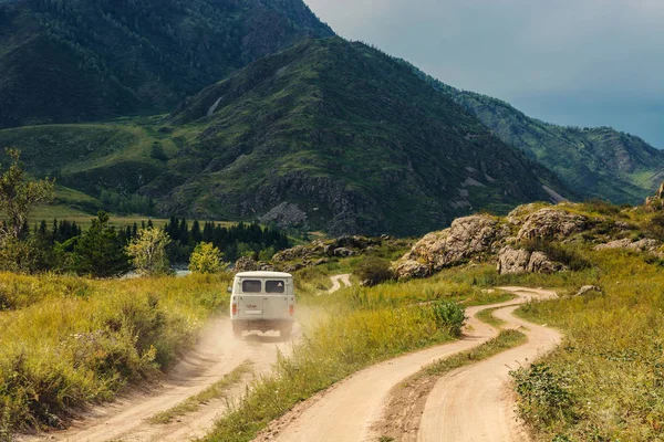 Araba dağlar ve tepeler arasında toprak bir yol boyunca ilerliyor. Dağ Altay.