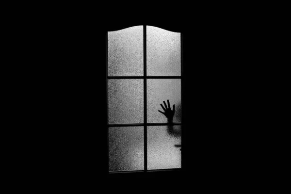 Dark silhouette of hand behind glass in supernatural light. Locked alone in room behind door on Halloween. Nightmare of kid with aliens, monsters and ghosts. Evil in home. hild inside haunted house