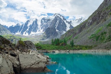 Dağ gölü dev güzel buzul önünde büyük taşlar ve kayalar ile çevrilidir. İnanılmaz karlı dağlar. Kar lı sırt. Yaylaların görkemli doğasının harika atmosferik manzarası.