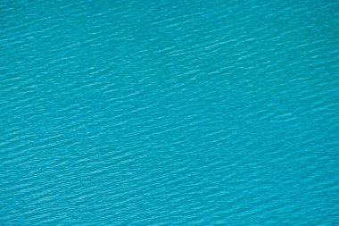 Sakin masmavi temiz su yüzeyinin inanılmaz dokulu arka planı. Dağ gölünde güneş ışığı yakın. Güneşli bir günde parlak suda güzel dalgalar. Harika rahatlayın doku.