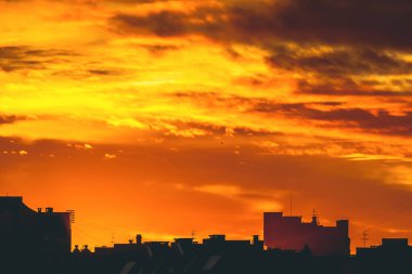 Cityscape canlı ateşli şafak ile. İnanılmaz sıcak dramatik bulutlu gökyüzü karanlık siluetleri şehir binaların yukarıda. Turuncu güneş ışığı. Gündoğumu bulutlu havalarda atmosferik arka plan. Kopya alanı.
