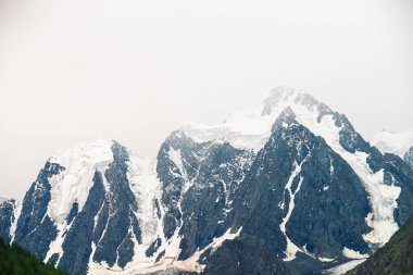 İnanılmaz büyük bir buzul tepesi. Bulutlu gökyüzünde karlı dağ sırası. Sis içinde kar ile harika dev kayalık sırt. Yaylaların görkemli doğasının atmosferik minimalist manzarası. Sakin dağ manzarası.