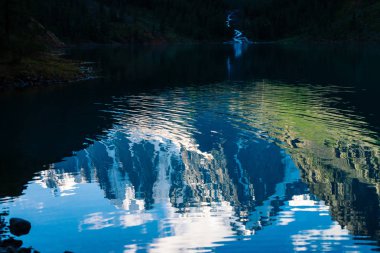 Dağ deresi göle akar. Harika buzuldan su akışı. Muhteşem karlı dağlar dağ gölüne yansıdı. Temiz parlak su. Yaylaların görkemli doğasının atmosferik manzarası.
