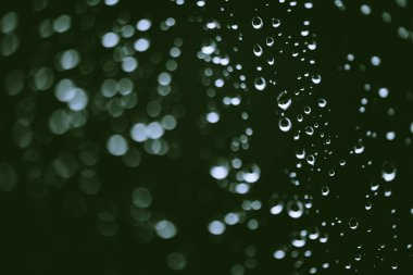 Yağmur damlalarıyla kirli pencere camı. Bokeh yağmur damlaları ile atmosferik yeşil arka plan. Damlacıklar ve lekeler kapanır. Kopyalama alanı ile makroda ayrıntılı saydam doku. Yağmurlu hava.