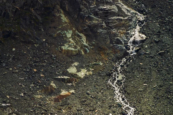 Detailed natural texture of slope from loose stones. Mountain water stream flows down mountainside. Small waterfall on rock. Unusual landscape of majestic nature.