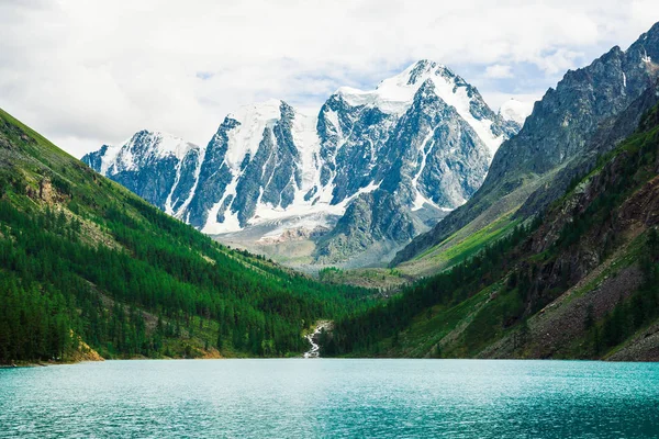 Wonderful giant snowy mountains. Creek flows from glacier into mountain lake. Shine water in highlands. White clear snow on ridge. Amazing atmospheric landscape of majestic nature.