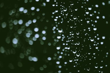 Yağmur damlalarıyla kirli pencere camı. Bokeh yağmur damlaları ile atmosferik yeşil arka plan. Damlacıklar ve lekeler kapanır. Kopyalama alanı ile makroda ayrıntılı saydam doku. Yağmurlu hava.