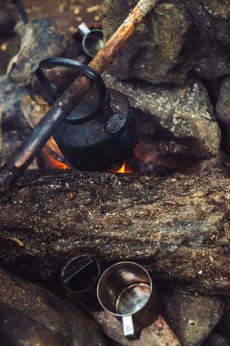 Büyük odun ile şenlik ateşinde su ısıtıcısı çay kaynatma. Açık havada çay içmek. Aktif açık hava rekreasyon. Gün batımında kamp. Doğada alacakaranlık romantik sıcak atmosfer. Aktif istirahat. Metal kupa.