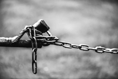 Çit zinciri üzerinde kapalı asma kilit kopya alanı ile bokeh ile asfalt arka plan üzerinde yakın çekim. Park yeri kilidi ile monokrom zemin. Denetim noktasının gri tonlamasındaki kontrast görüntüsü.