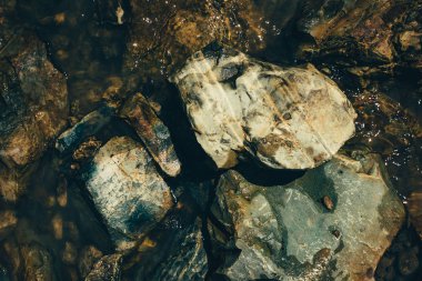 Su yakın çekimçiğ cevheri. Güneş ışığında çok renkli ıslak pürüzlü taşlar. Kaba taş yığını ile dokulu canlı jeolojik arka plan. Kopyalama alanı ile doğal doku. İnanılmaz bir mineral. Kaya parçası.