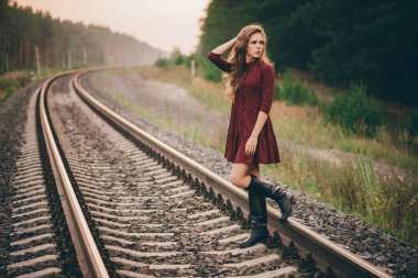 Demiryolu üzerinde ormanda doğada kıvırcık doğal saçları ile Güzel üzgün düşünceli kız. Bordo elbiseli hayalperest bayan demiryolunda yürüyor. Şafakta rayların üstünde ki depresif kız. Sonbaharda saçta güneş. Kötü ruh hali.