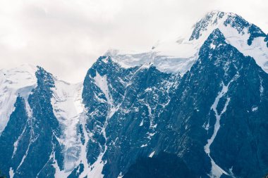 İnanılmaz büyük bir buzul tepesi. Bulutlu gökyüzünde karlı dağ sırası. Sis içinde kar ile harika dev kayalık sırt. Yaylaların görkemli doğasının atmosferik minimalist manzarası. Sakin dağ manzarası.