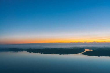 Geniş nehir kalın sis altında orman ile diyagonal kıyı boyunca akar. Erken mavi gökyüzü suya yansıdı. Pitoresk şafak öncesi gökyüzünde sarı parıltı. Görkemli doğanın renkli sabah atmosferik manzara