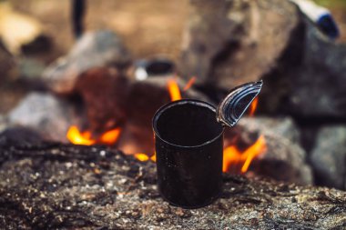 Büyük yakacak odun ile şenlik ateşinde metal kupa çay ısıtma. Açık havada çay içmek. Aktif açık hava rekreasyon. Gün batımında kamp. Doğada alacakaranlık romantik sıcak atmosfer. Aktif dinlenme.
