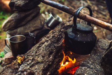 Büyük odun ile şenlik ateşinde su ısıtıcısı çay kaynatma. Açık havada çay içmek. Aktif açık hava rekreasyon. Gün batımında kamp. Doğada alacakaranlık romantik sıcak atmosfer. Aktif istirahat. Metal kupa.