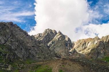 Tepenin üstünde dev bir bulut. Bitki örtüsü ile alışılmadık kayalık dağ. Mavi bulutlu gökyüzü altında Amazing dağ aralığı. Harika kayalar. Yaylaların görkemli doğasının atmosferik manzarası.