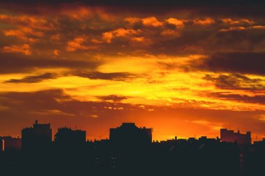 Cityscape canlı ateşli şafak ile. İnanılmaz sıcak dramatik bulutlu gökyüzü karanlık siluetleri şehir binaların yukarıda. Turuncu güneş ışığı. Gündoğumu bulutlu havalarda atmosferik arka plan. Kopya alanı.