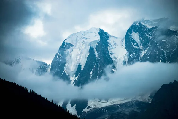 巨大な氷河の前に低い雲 曇り空の下に巨大な雪の岩山 早朝の森の上の山々の濃い霧 不可解な霧暗い大気の風景 静かな雰囲気 — ストック写真