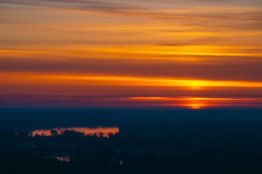 Büyük kırmızı güneş çemberi gölün üzerinde sıcak tonları arka plan varicolored bulutlar üzerinde karanlık ufuk arkasından yükselir. Pitoresk bulut gökyüzü ve nehir üzerinde şafak güzel arka plan.