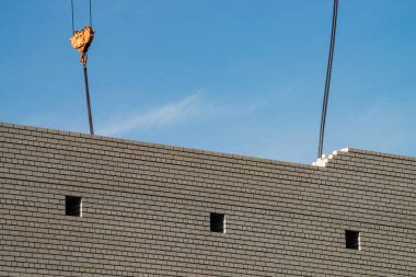 Şantiyede bitmemiş binanın üzerinde kule vinç kanca. Mavi gökyüzü altında beyaz tuğla duvar arka plan görüntüsü. İşlem oluşturmanın arka plan görüntüsü.