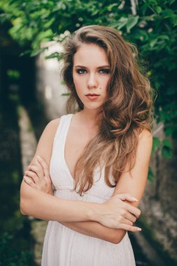 Yeşil ağaç yaprakları yakınında beyaz elbise kıvırcık doğal saçlı güzel huysuz kız. Yaz güzellik portresi. Doğadaki üzgün bayan dışarıda. Ormanda uzun tünelde dalgın görme ile Yalnız ciddi kadın