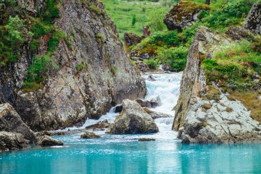 Dağ deresi masmavi göle akar. Hızlı dere akıntısı. Pürüzsüz su yüzeyi. Yaylaların zengin bitki örtüsü ile harika kayalar. Görkemli doğanın muhteşem manzarası.