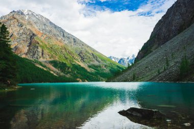 Kar ile büyük kayalık dağ yakınında dağ gölü. Güzel bir buzul. İnanılmaz dev karlı sırt. Kayalar temiz parlak suda. Yaylaların görkemli doğasının harika atmosferik manzarası.