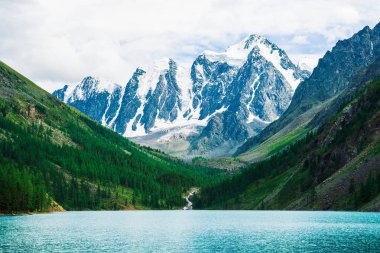 Muhteşem, dev, karlı dağlar. Nehir buzuldan dağ gölüne akar. Dağlık arazide parlayan su. Tepede beyaz kar var. Muhteşem atmosferik Altai doğası..