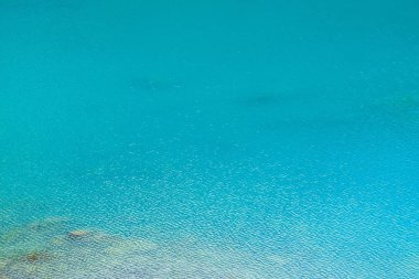 Sakin masmavi temiz su yüzeyinin inanılmaz dokulu arka planı. Dağ gölünde güneş ışığı yakın. Güneşli bir günde parlak suda güzel dalgalar. Harika rahatlayın doku.