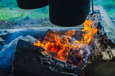Şenlik ateşinin üstünde kazan ve su ısıtıcısı. Doğada yemek pişirmek. Dışarıda akşam yemeği. Odun ve dalları ateşte. Aktif istirahat. Ormanda kamp.