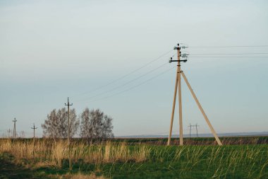 Mavi gökyüzü altında ağaçların arka planda toprak yol ile yeşil alanda güç hatları ile atmosferik manzara. Kopyalama alanı olan elektrik direkleri. Yerden yüksek voltajlı kablolar. Elektrik endüstrisi.
