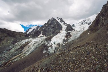 Bulutlu gökyüzü altında karlı dev dağ aralığı. Kar lı kayalık sırt. Büyük bir buzul. Su akıntıları ile buzlu dağ. Harika dağlar. Doğanın atmosferik minimalist dağlık manzara.