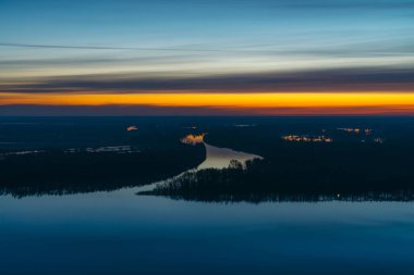 Şafak öncesi gökyüzünün altında ağaçlar ile büyük ada ile güzel nehir. Pitoresk bulutlu gökyüzünde parlak sarı şerit. Erken mavi gökyüzü suya yansıdı. Görkemli doğanın renkli sabah atmosferik görüntüsü.