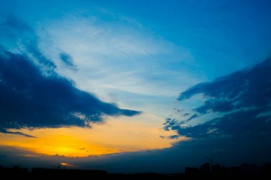 Şehir binalarının siluetleri arkasında atmosferik mavi bulutlu gökyüzü. Kobalt ve kopya alanı için yoğun bulutlar ve parlak sarı güneşli ışık ile gündoğumu turuncu arka plan. Bulutların üzerindeki Siyam cenneti.