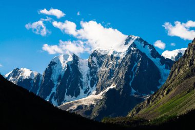 Mavi gökyüzünün altında inanılmaz bir buzul. Güneş ışığında dev harika karlı dağlarda dev bulut. Zengin bitki örtüsü ve yayla ormanı. Güneşli bir günde görkemli doğanın atmosferik minimalist manzara.