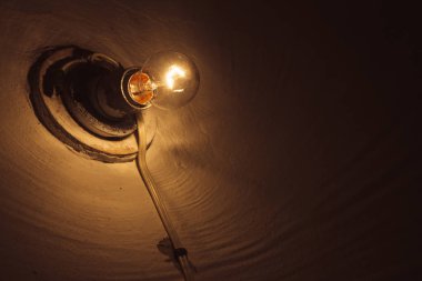 Akkor lamba karanlık oda yakın çekim içinde yanar. Kopyalama alanı ile aydınlatma. Pürüzlü duvarda eski ampul. Lamba bodrumu aydınlatın. Karanlıkta ışık. Minimalist arka plan. Sıcak turuncu aydınlatma.
