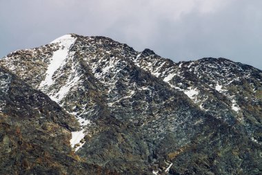 Bulutlu gökyüzünde karlı dağ başı. Bulutların altındaki kayalık sırt. Dağlık bölgelerde bulutlu hava. Görkemli doğanın atmosferik minimalist manzara.