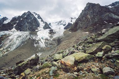 Bulutlu gökyüzü altında karlı dev dağ aralığı. Kar lı kayalık sırt. Büyük bir buzul. Su akıntıları ile buzlu dağ. Harika dağlar. Doğanın atmosferik minimalist dağlık manzara.