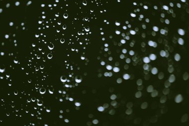 Yağmur damlalarıyla kirli pencere camı. Bokeh yağmur damlaları ile atmosferik yeşil arka plan. Damlacıklar ve lekeler kapanır. Kopyalama alanı ile makroda ayrıntılı saydam doku. Yağmurlu hava.