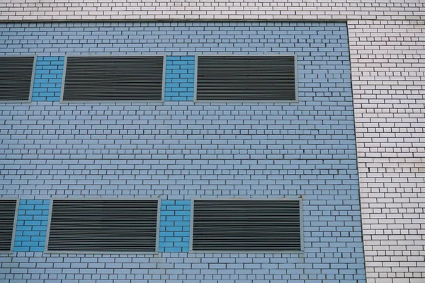 Wall of cooperative building for store, workshop, garage and other industrial needs. Background from white brick wall with metallic closed windows and insertions of blue brick close-up with copy space
