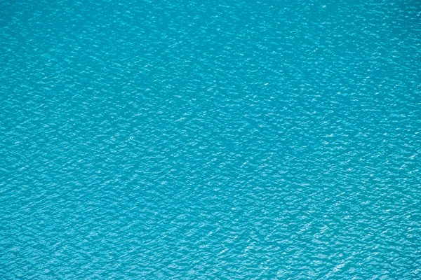 Amazing textured background of calm azure clean water surface. Sunshine in mountain lake close up. Beautiful ripples on shiny water in sunny day. Wonderful relax texture.
