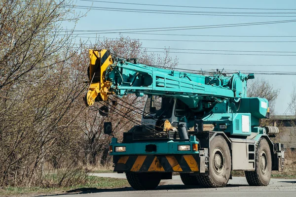 Large heavy car with crane is driving along road under wires.